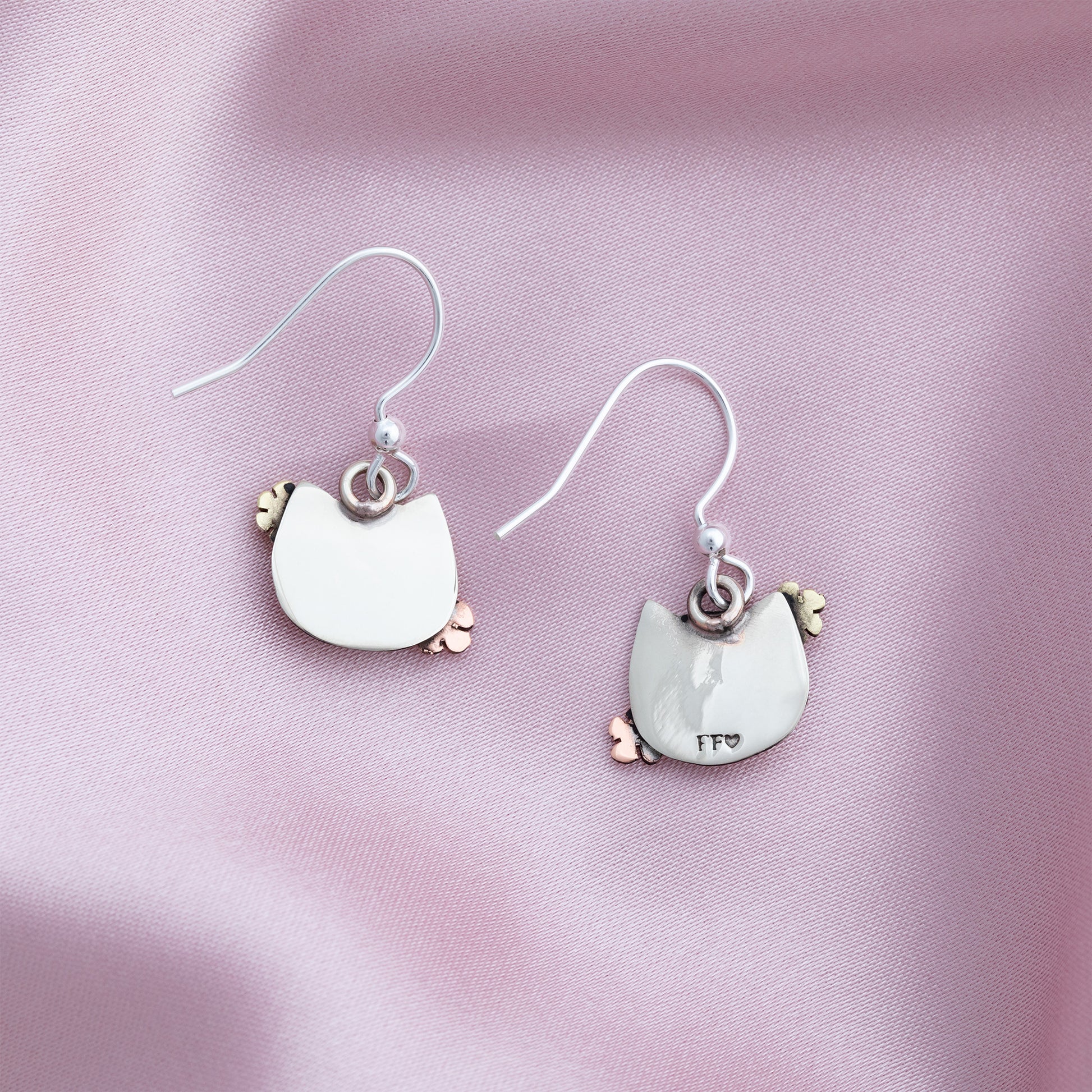 The backs of cat-shaped earrings on a pink fabric background