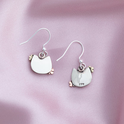 The backs of cat-shaped earrings on a pink fabric background