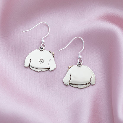 The backs of silver dog-shaped earrings on a pink satin background