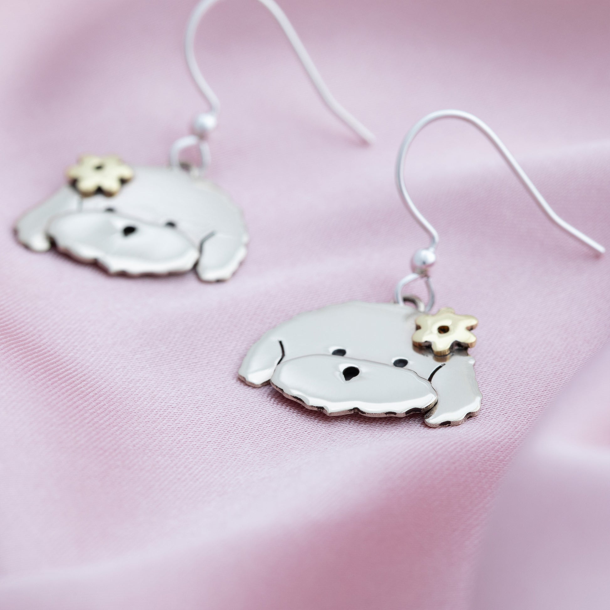 Silver dog-shaped earrings on a pink fabric background