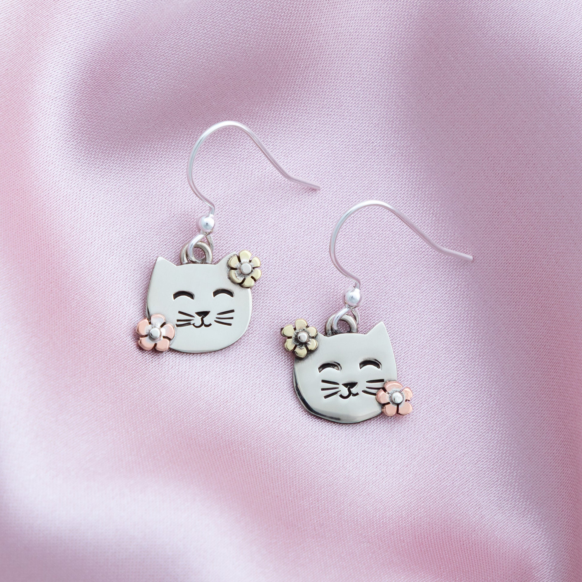 Cat-shaped earrings with floral details on a pink satin background
