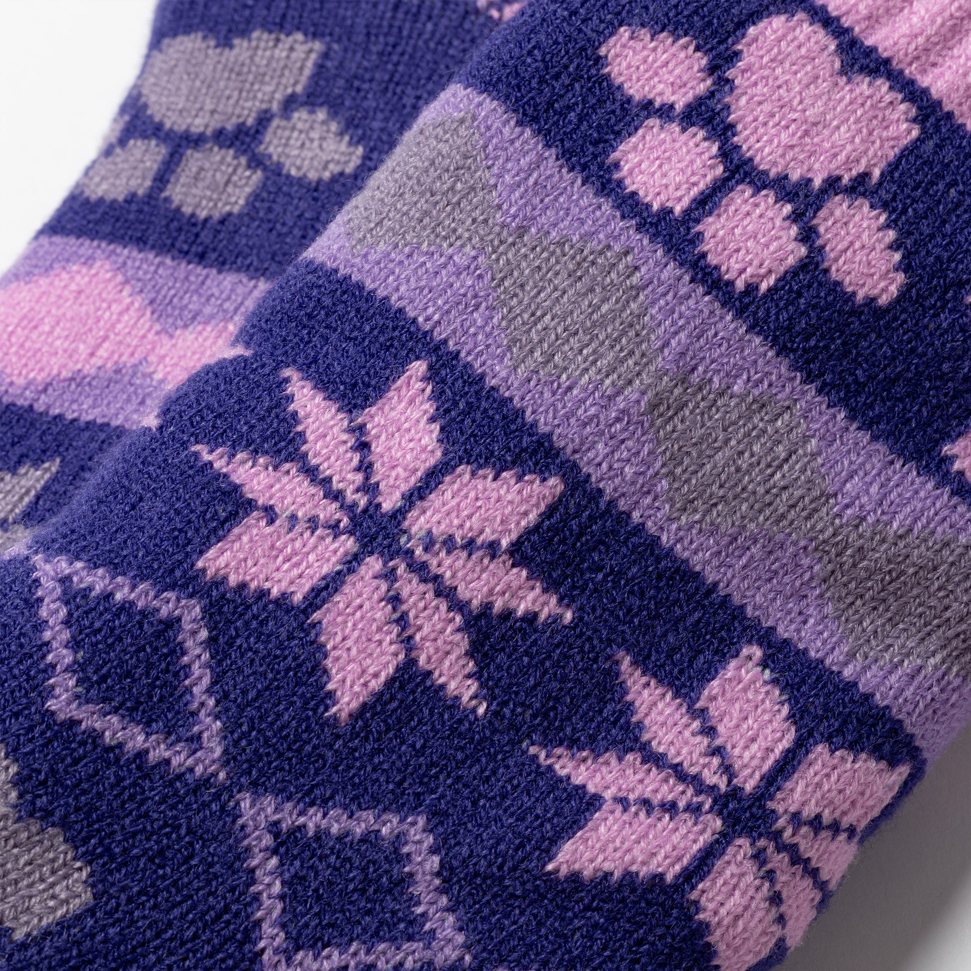 close up of detail  of knitted fabric Pair of pink, gray purple Sherpa Fleece Lined Paw Print Cabin Slipper Socks with sherpa trim on a light gray background alpine fair isle paws plum