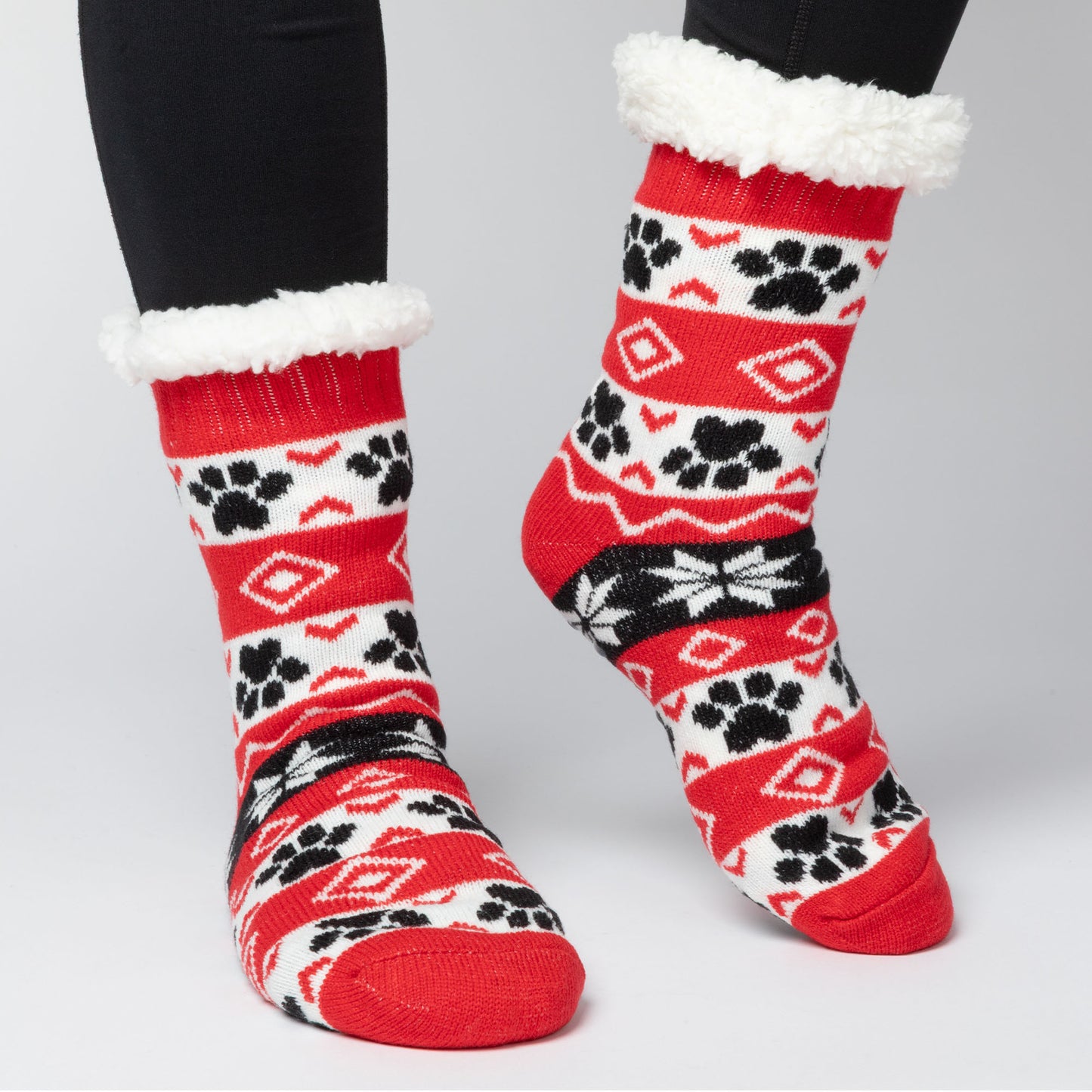 model wearing Pair of red, black white Sherpa Fleece Lined Paw Print Cabin Slipper Socks with sherpa trim on a light gray background alpine fair isle paws red 