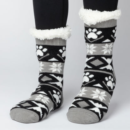 Model wearing Pair of gray, black white Sherpa Fleece Lined Paw Print Cabin Slipper Socks with sherpa trim on a light gray background alpine fair isle paws black