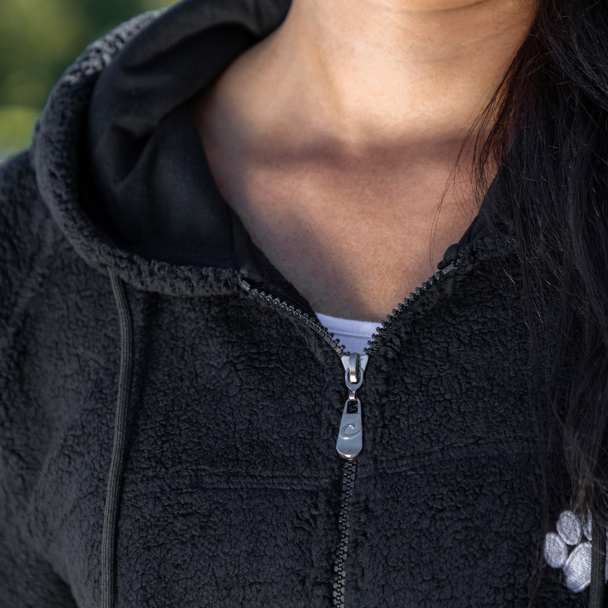 Close up of a zipper and drawstring hood on a black sherpa fleece jacket, worn by a person.
