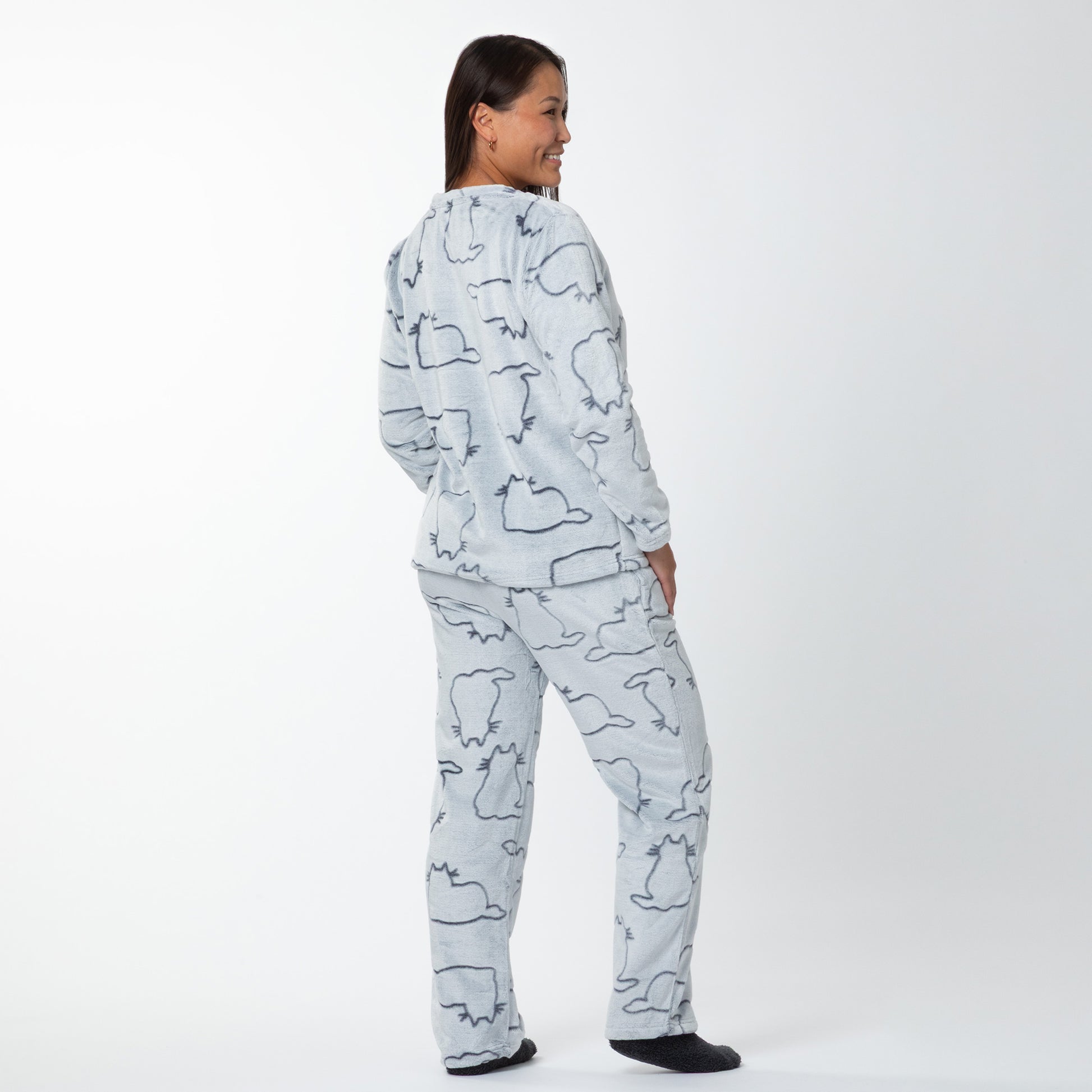 A woman wearing a matching set of fluffy, soft long-sleeve pajamas. The top and pants are light grey and patterned with cute cat outlines. She is showing the back if the long-sleeve top and pants.