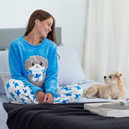 A woman sitting on a bed smiling at her pet dog. She is wearing a blue long-sleeve top with an embroidered cute dog design and gray, blue and light blue houndstooth pattern. Design a grey dog with a scarf in super cozy fabric.