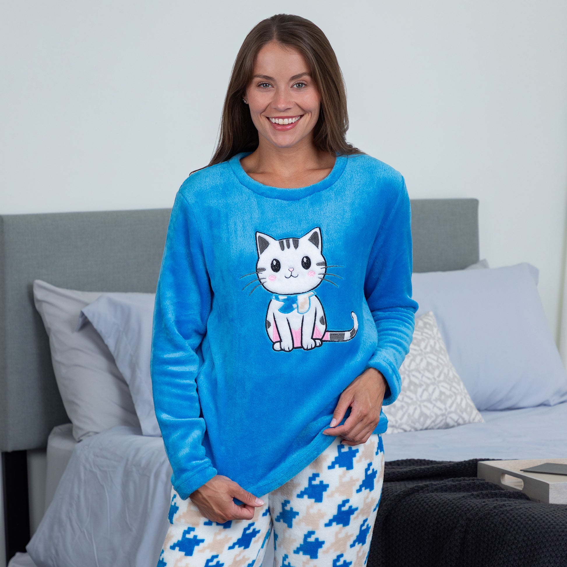 A woman wearing a blue long-sleeve top with an embroidered cute cat design and gray, blue and light blue houndstooth pattern. Design a blue cat in super cozy fabric