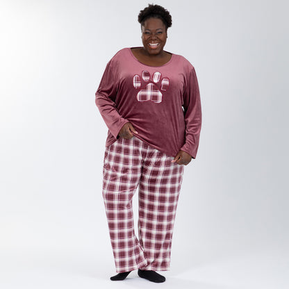 Woman wearing a velour pajama set— the top is a maroon long-sleeve shirt with a large plaid paw print. The pants are the same white and maroon plaid pattern as the paw print on the shirt. She is lifting one side of the hem to show how stretchy and forgiving the fabric of the shirt is. Extended and pus size available. 