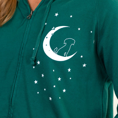 A close-up of a person wearing a teal green zip-up hoodie with a white graphic of a crescent moon, stars, and a dog silhouette on the chest.