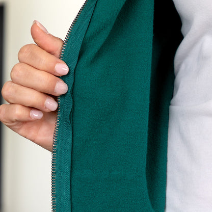 Close-up of a person's hand unzipping a dark teal green zippered jacket, showing the interior fleece lining and a white shirt underneath.