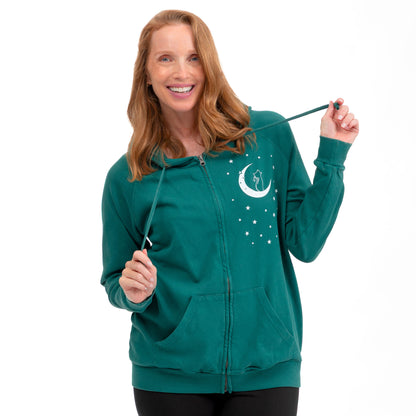 A woman wearing a teal green zip-up hoodie with a white crescent moon and stars graphic on the left chest, holding the drawstrings against a plain white background.