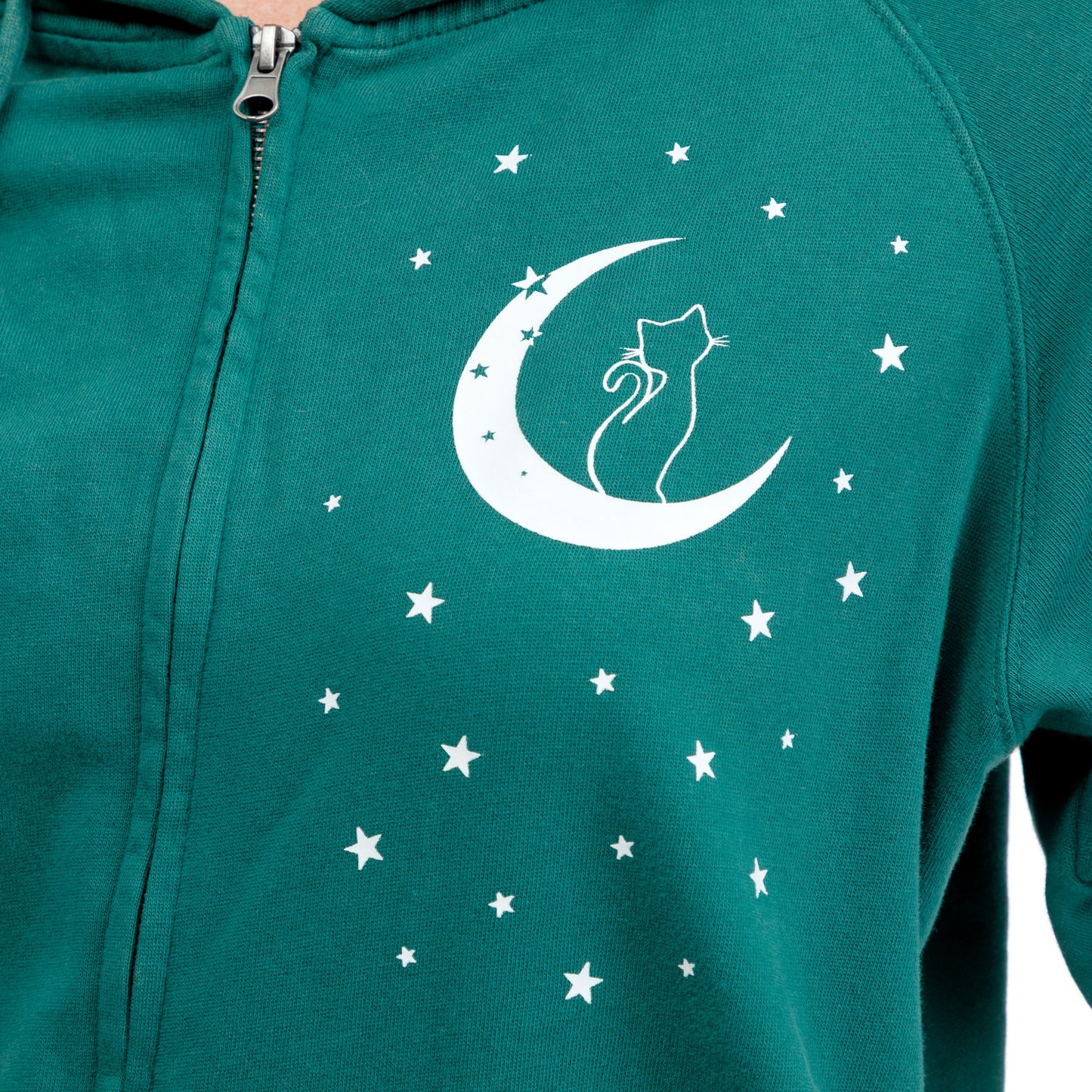 A close-up of a teal green zip-up hoodie featuring a white graphic of a cat sitting on a crescent moon, surrounded by small white stars.