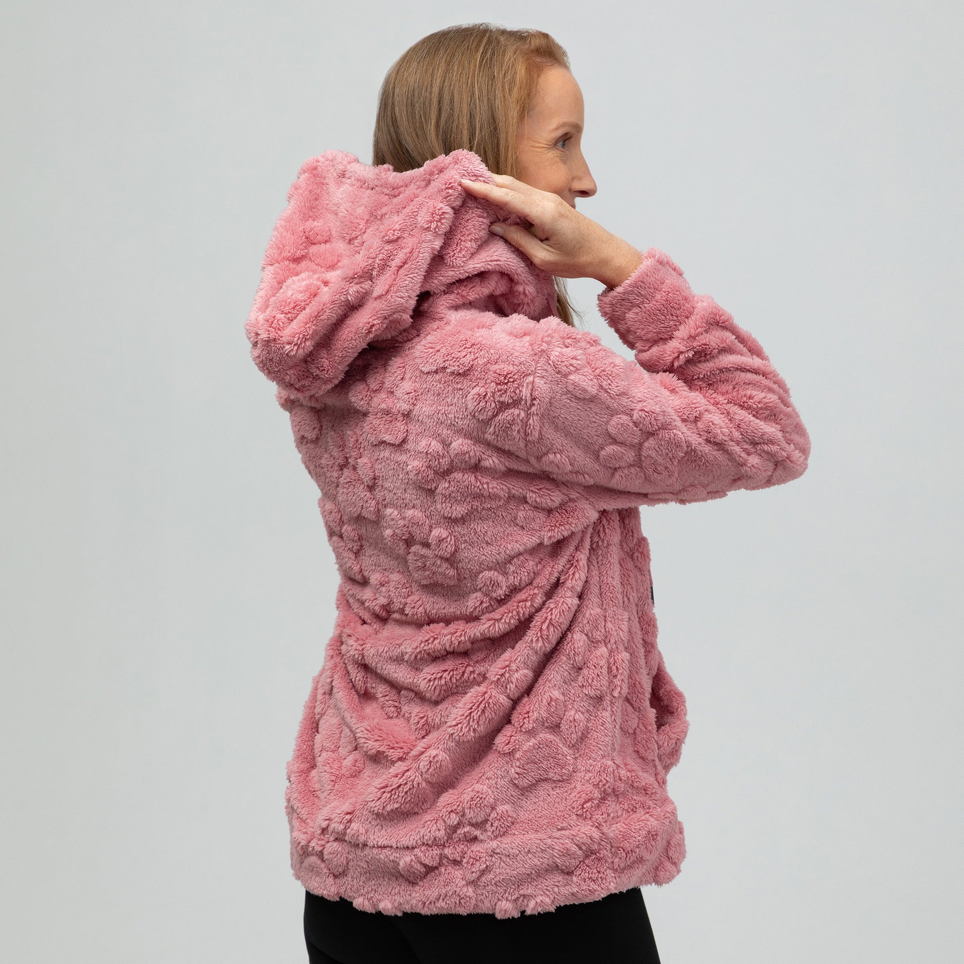 Woman wearing a pink paw print textured hoodie with a kangaroo pocket, and a white background.
