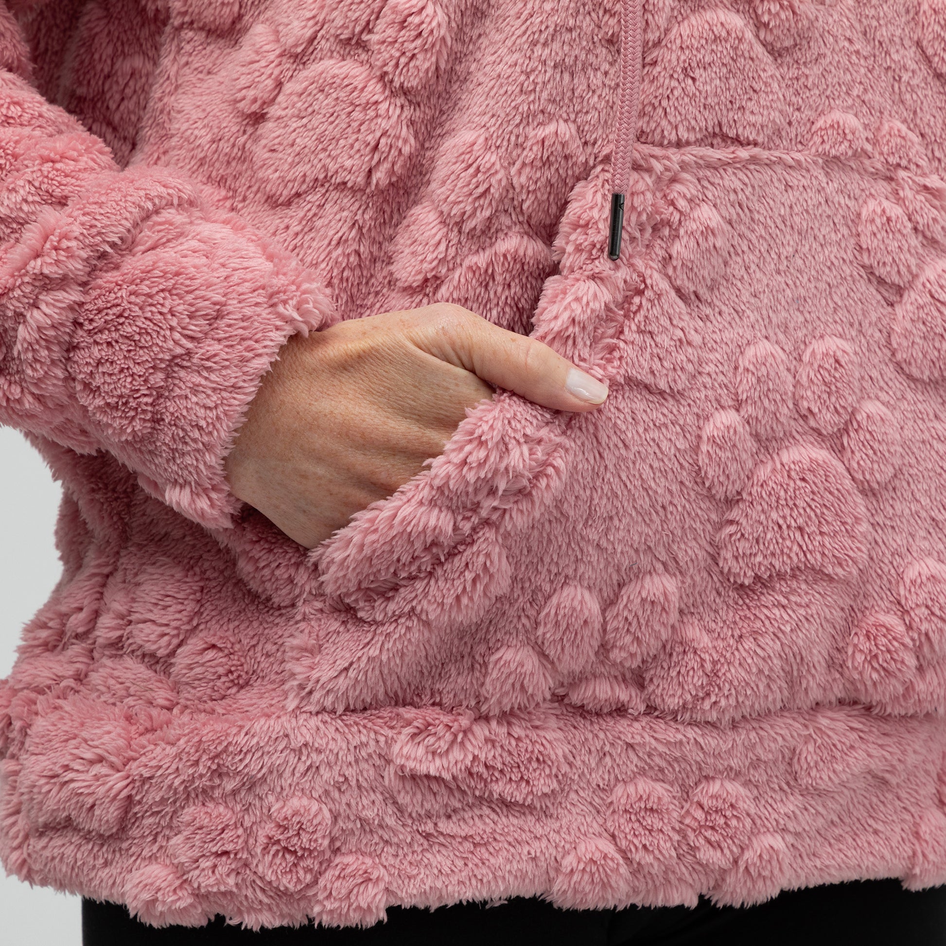 Close-up of a pink textured fleece hoodie with a hand reaching into the kangaroo pocket.