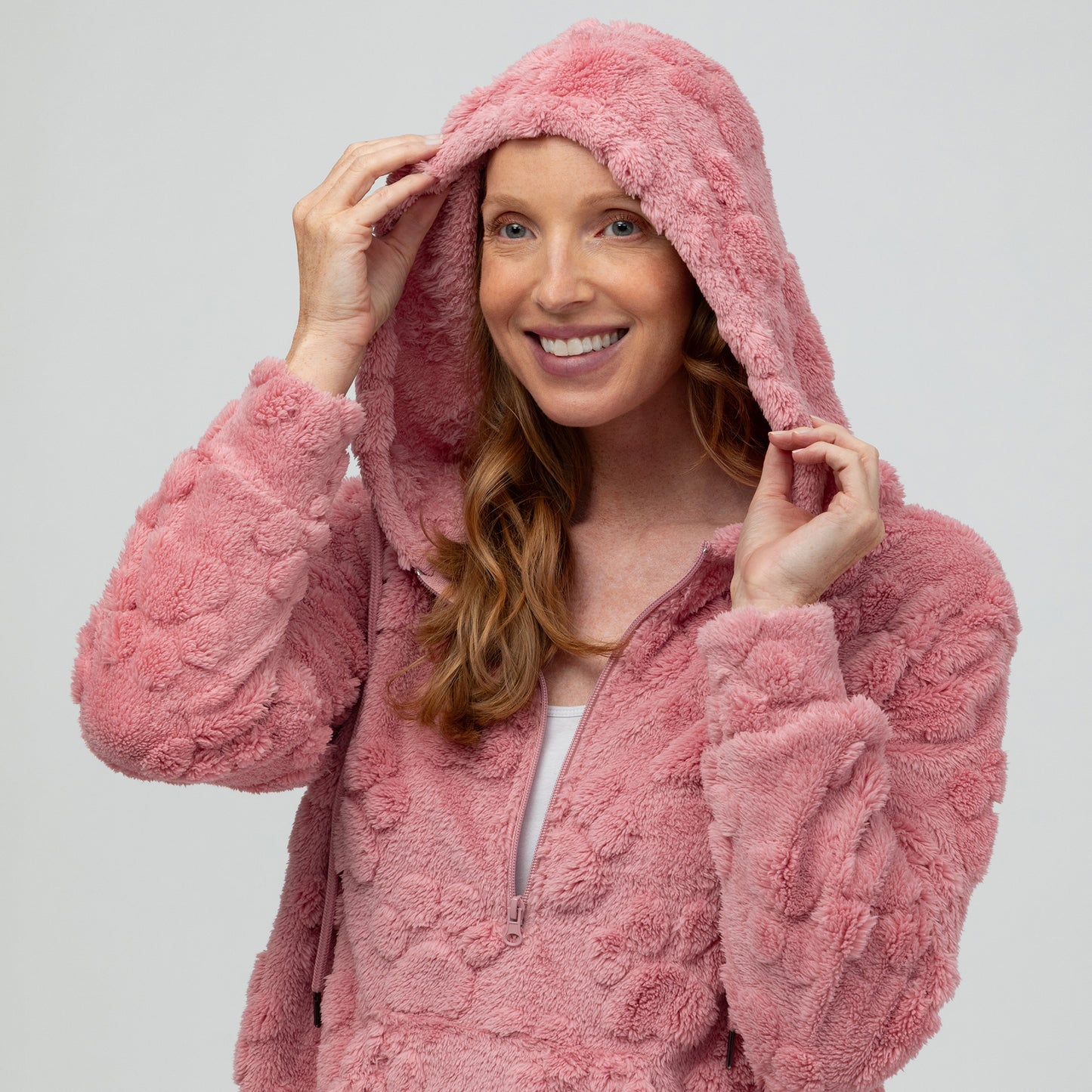 Woman wearing a pink fluffy paw print fleece hoodie against a white background