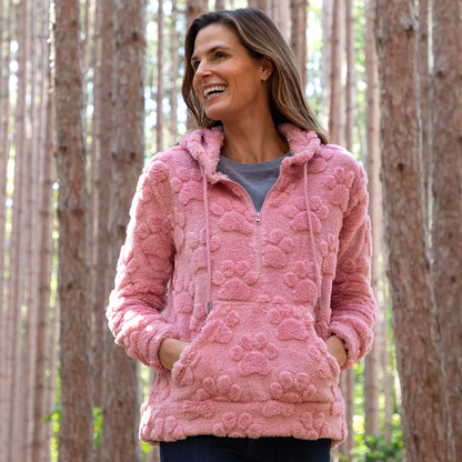 Woman wearing a pink textured hoodie with paw prints on it, standing in a forest.