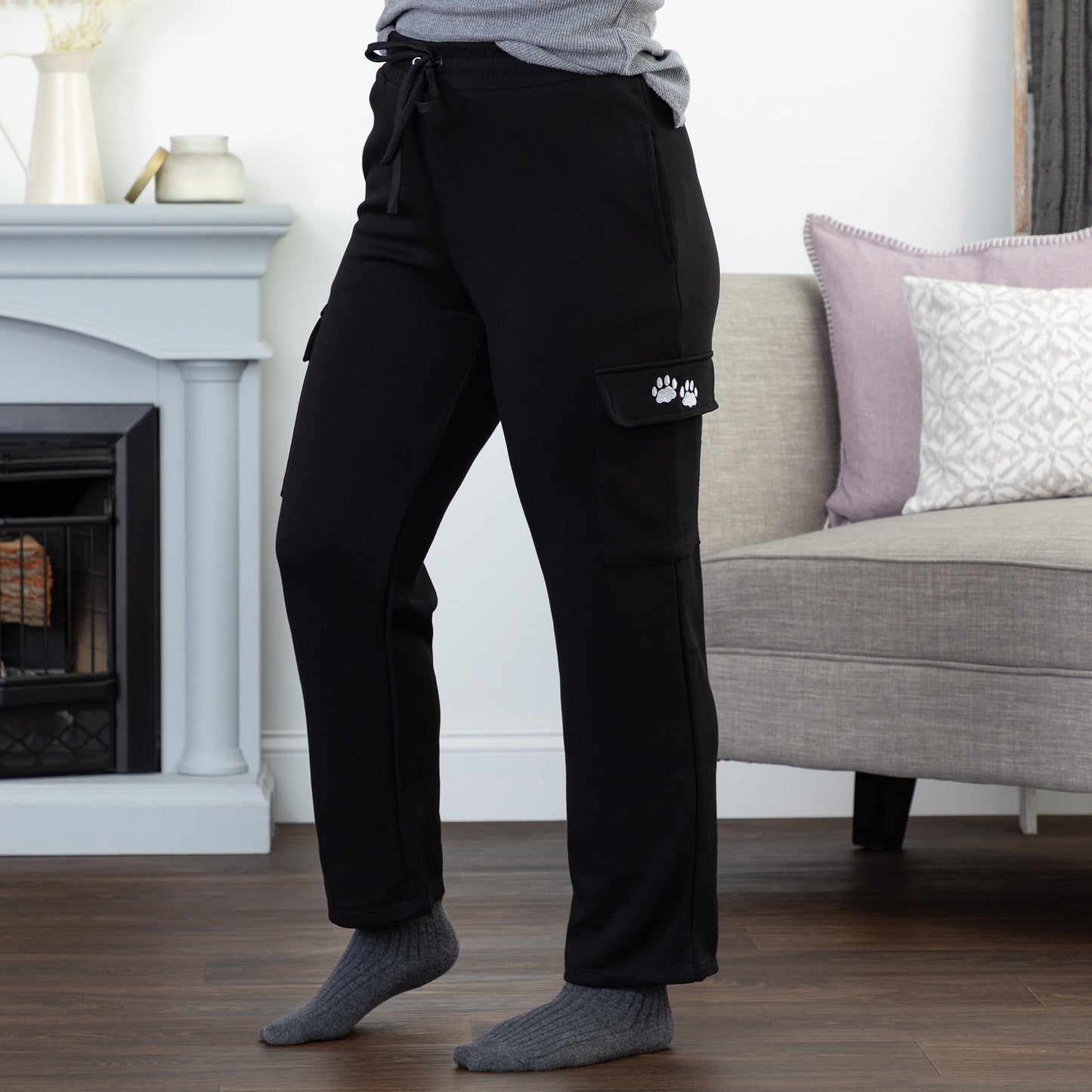Person wearing black cargo pants with two embroidered paws on the pocket, in a living room setting.
