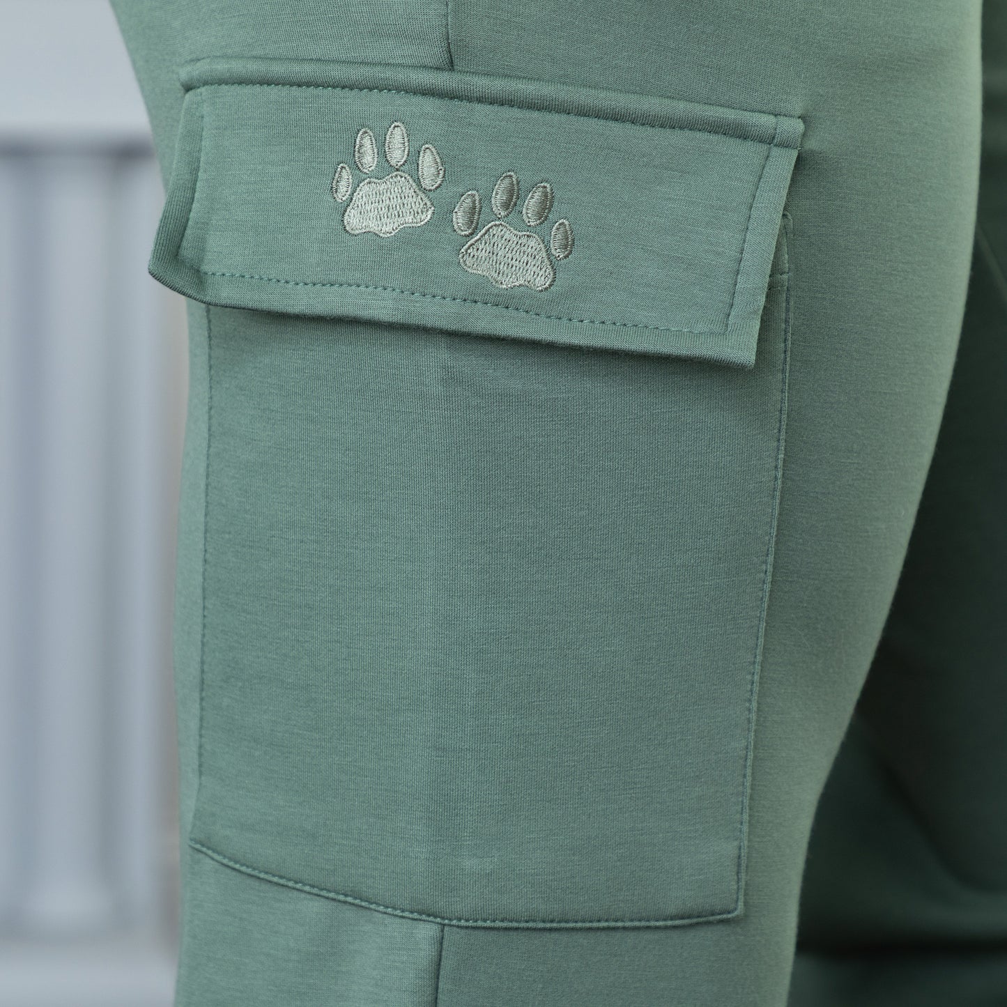 Close up of green embroidered paw prints on the pocket of a pair of green cargo pants.