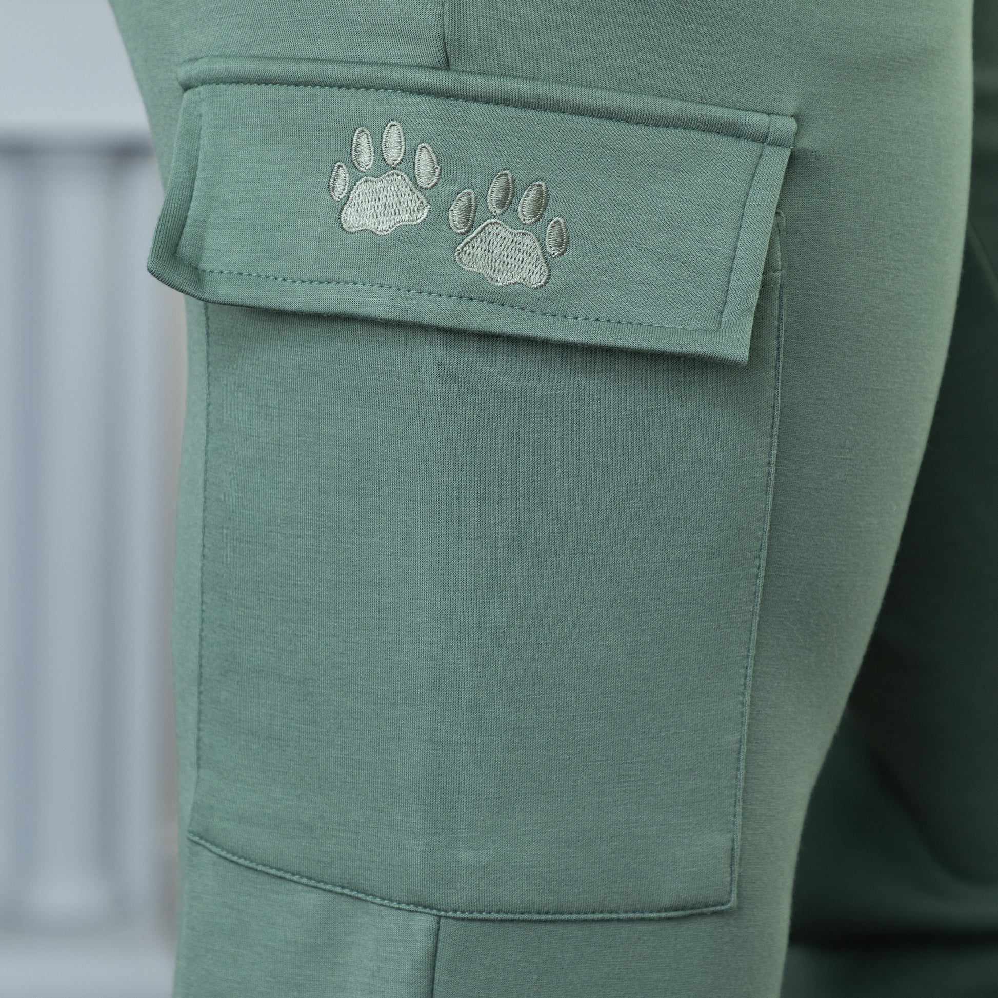 Close up of green embroidered paw prints on the pocket of a pair of green cargo pants.