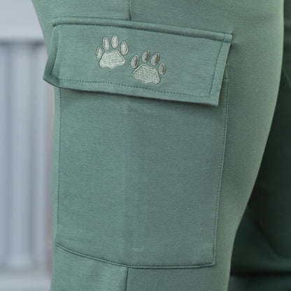 Close up of green embroidered paw prints on the pocket of a pair of green cargo pants.