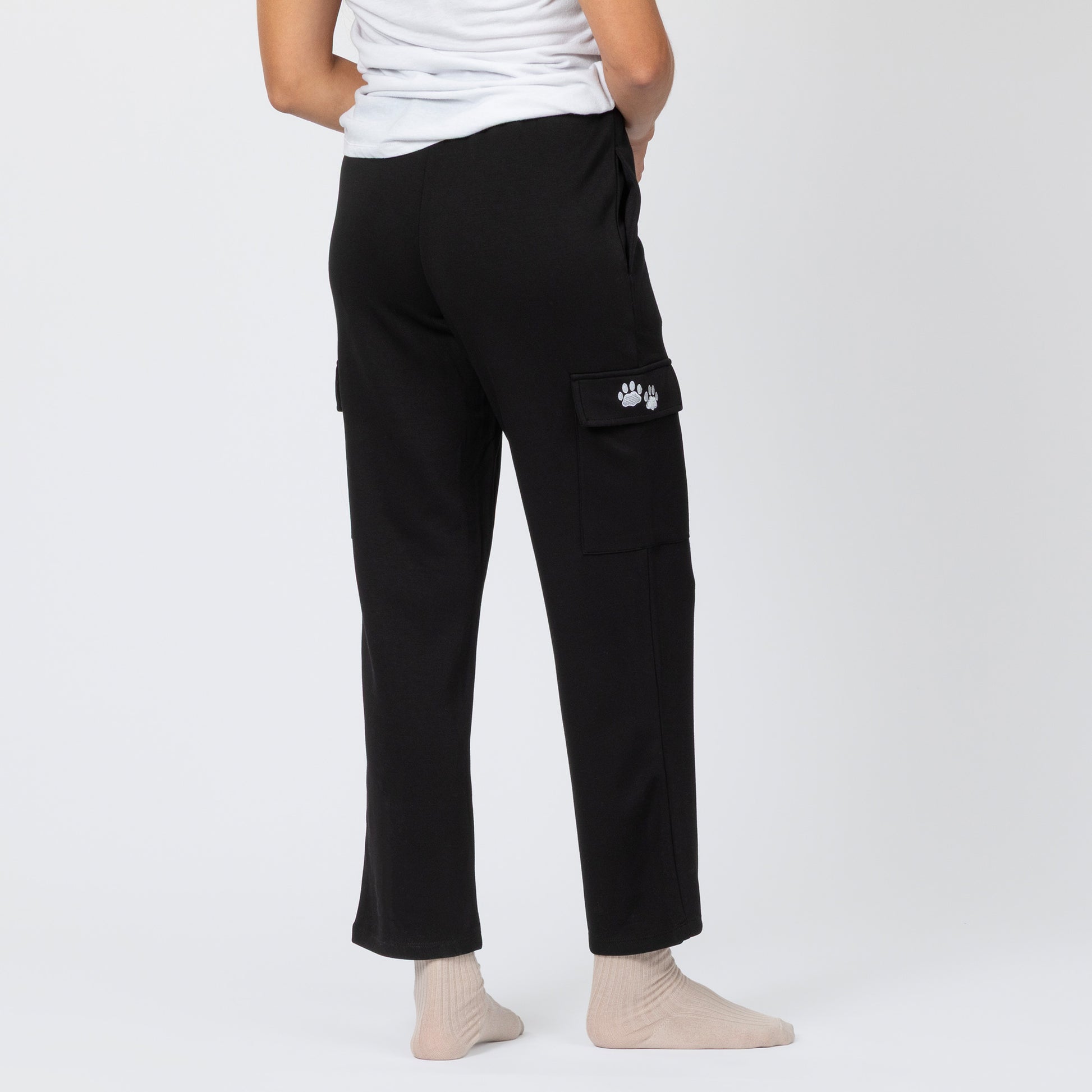 Person wearing black cargo pants with a paw print pocket on a white background