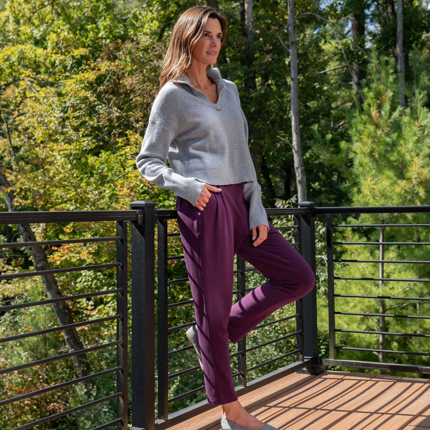 Woman standing on a wooden deck with greenery in the background, wearing plum colored Paw Print Pleated Panel Casual Pants with Pockets.