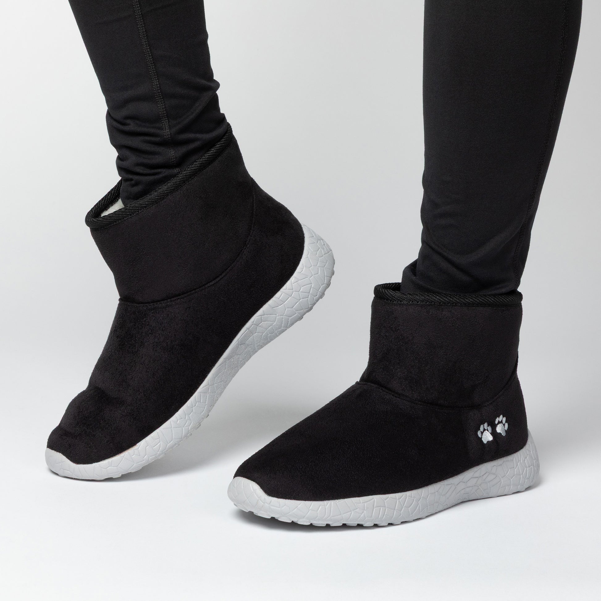 Black slip-on boots with white soles worn by a person on a light gray background