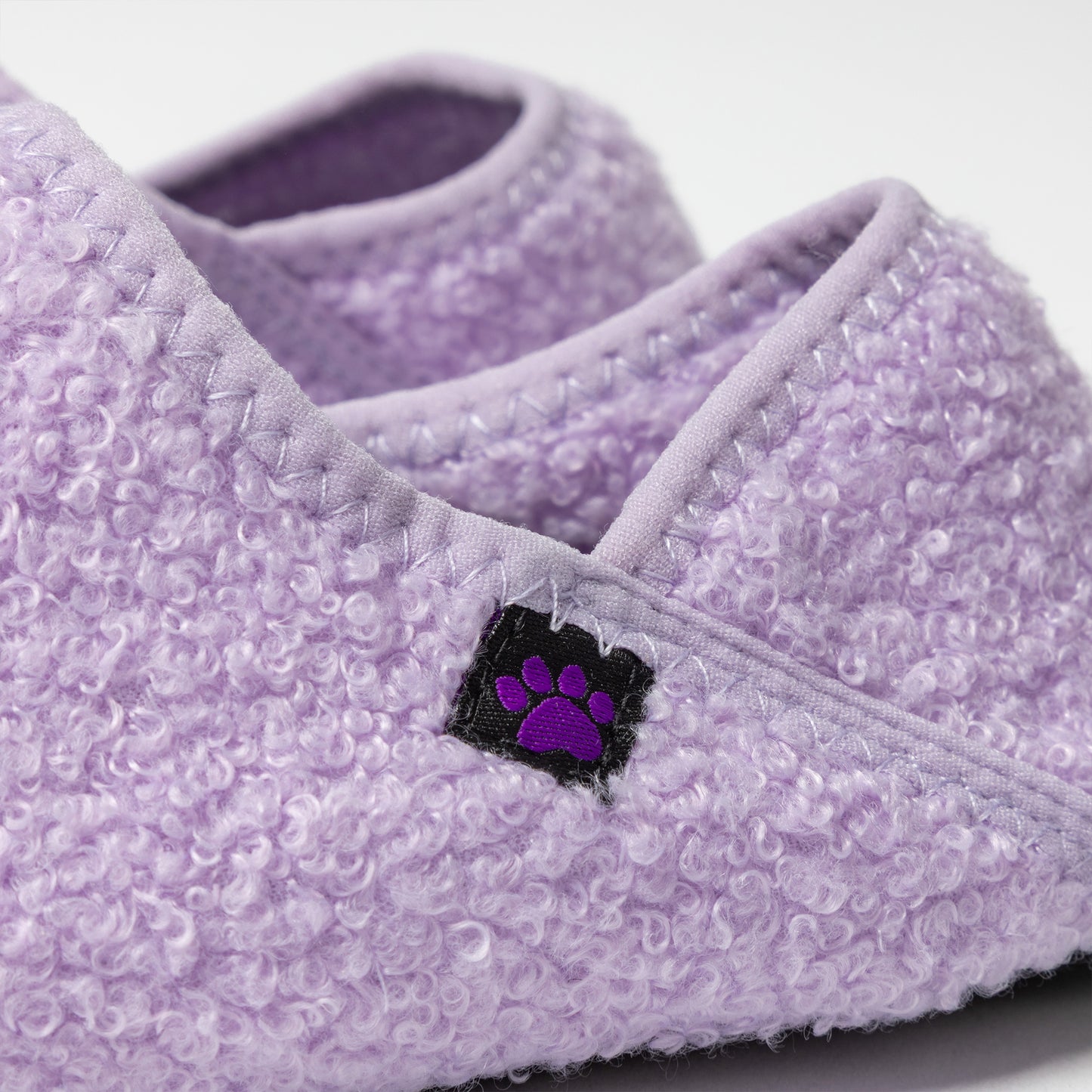 Close-up of purple textured slippers with a paw print logo on a light gray background