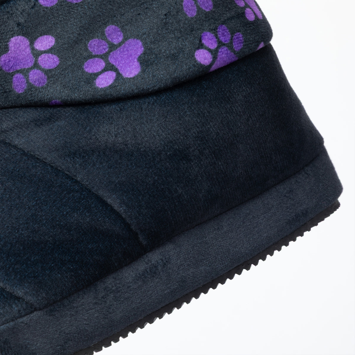 Close-up of a black slipper bootie showing the side profile, textured fabric upper, and a pattern of purple paw prints on the top edge against a white background.