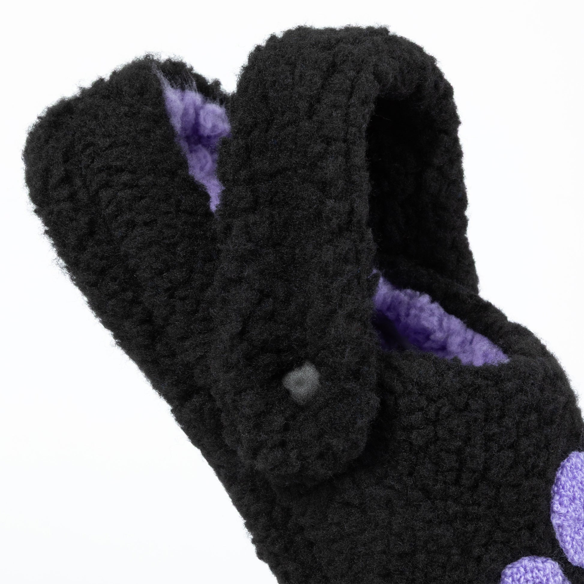 Black fuzzy slippers with purple interior on a white background