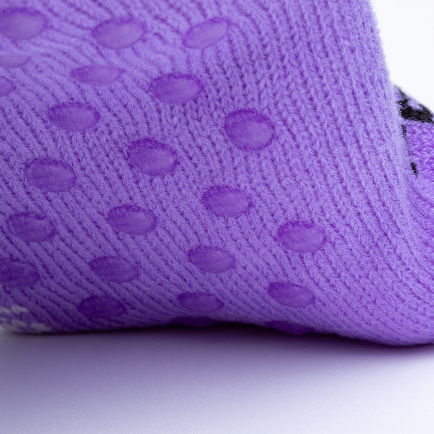 Close-up of a purple slipper sock bottom with traction dots on a white background