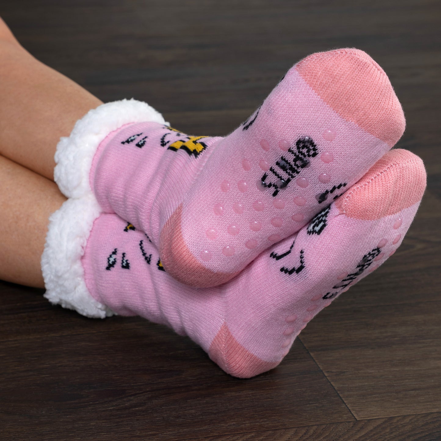 Pink slipper socks with text and white cuffs on a wooden floor