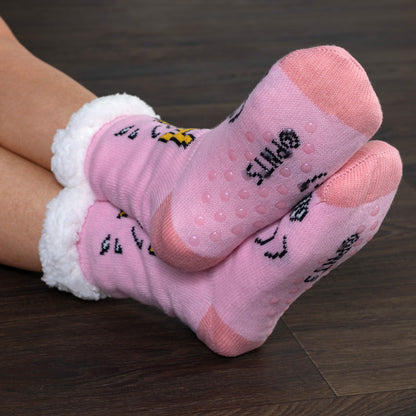 Pink slipper socks with text and white cuffs on a wooden floor