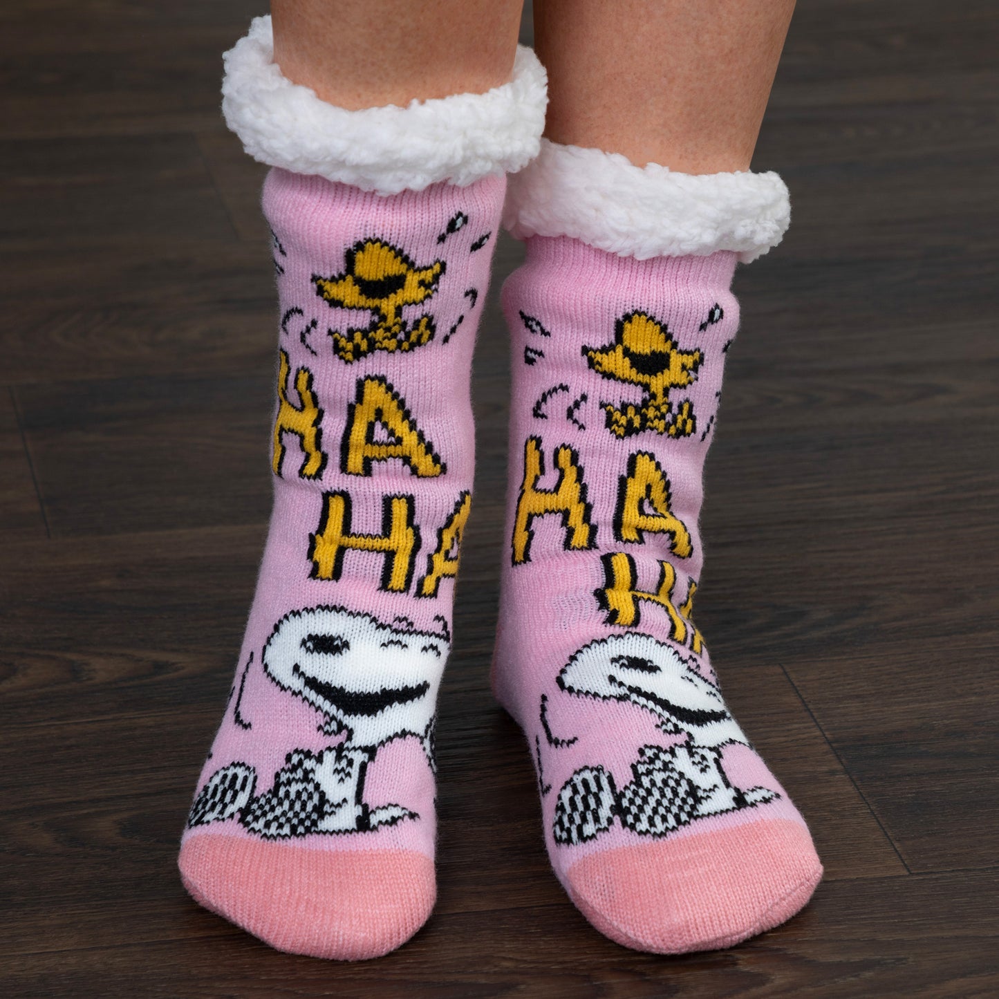 Pink socks with cartoon characters and 'HA HA HA' text on a wooden floor.