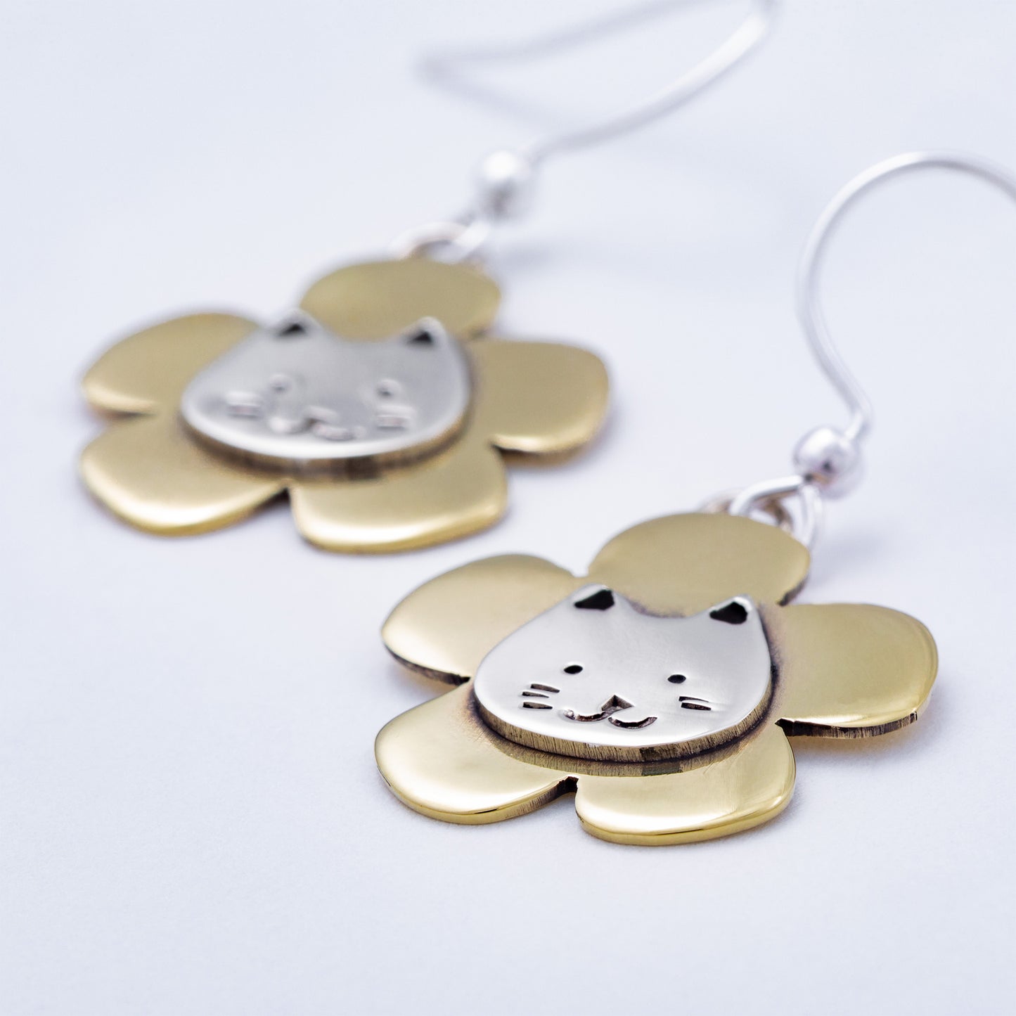 Brass and silver earrings with cat face designs on a white background
