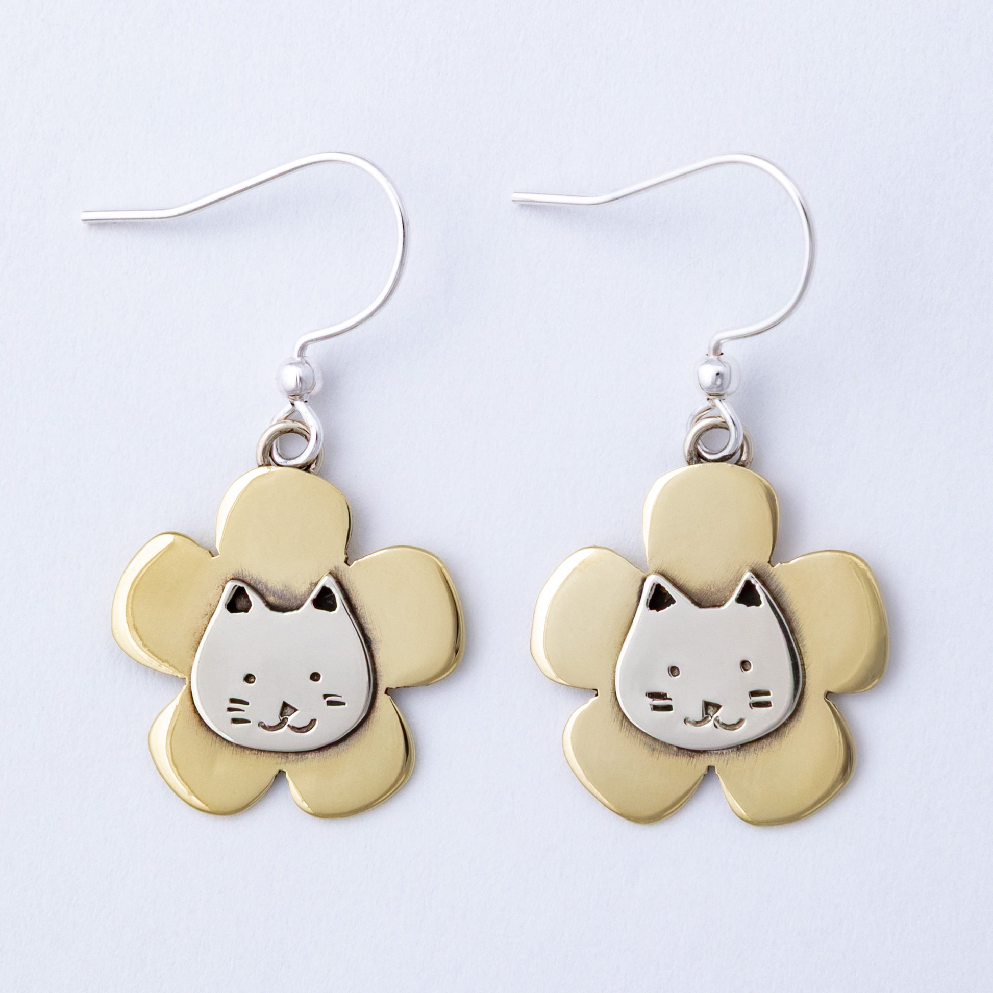 Flower-shaped earrings with cat face design on a light gray background