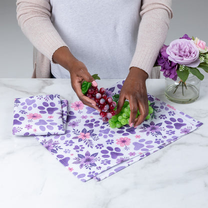 Person holding grapes and green grapes on a floral-patterned cloth with a vase of flowers in the background.