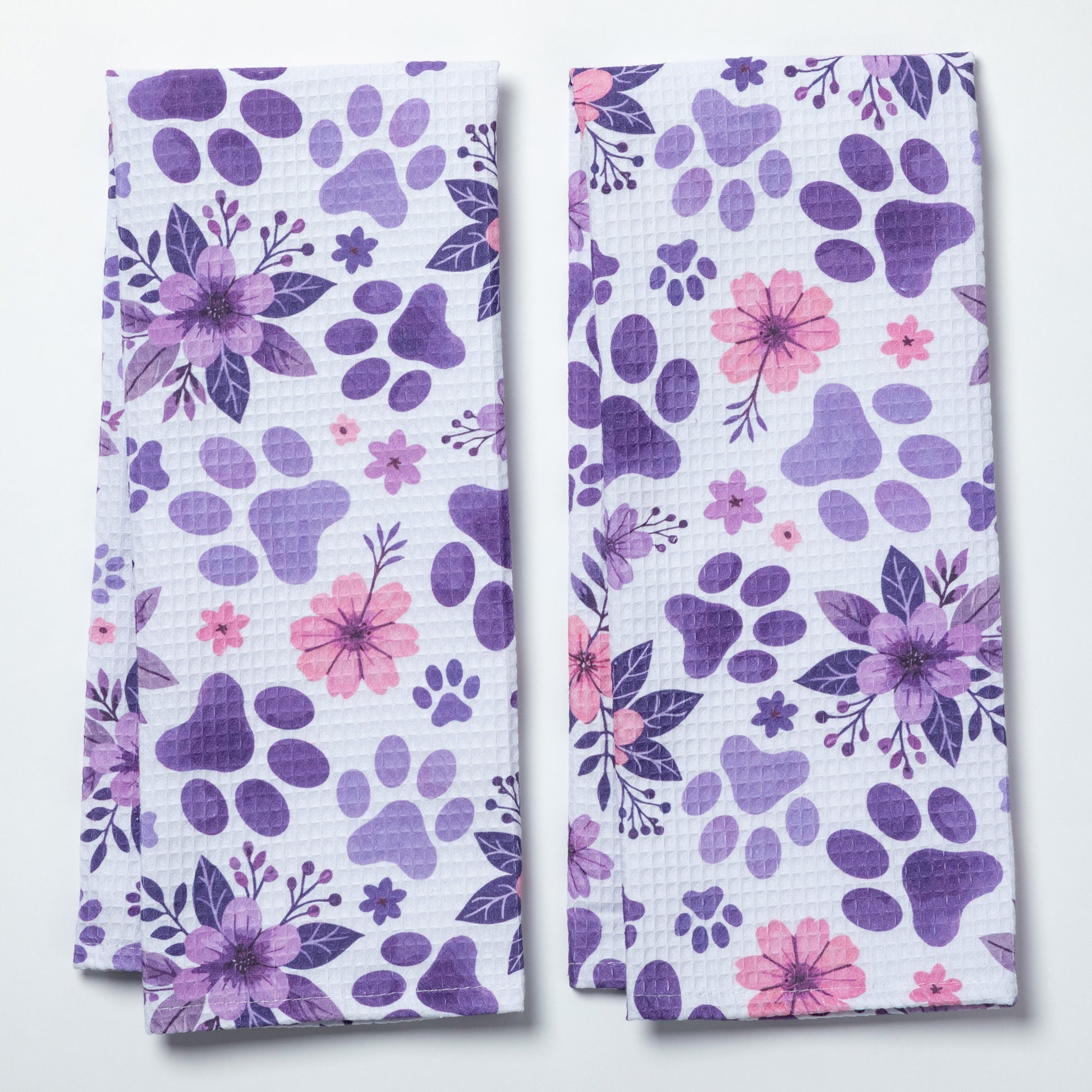 Two purple floral and paw print patterned kitchen towels on a white background