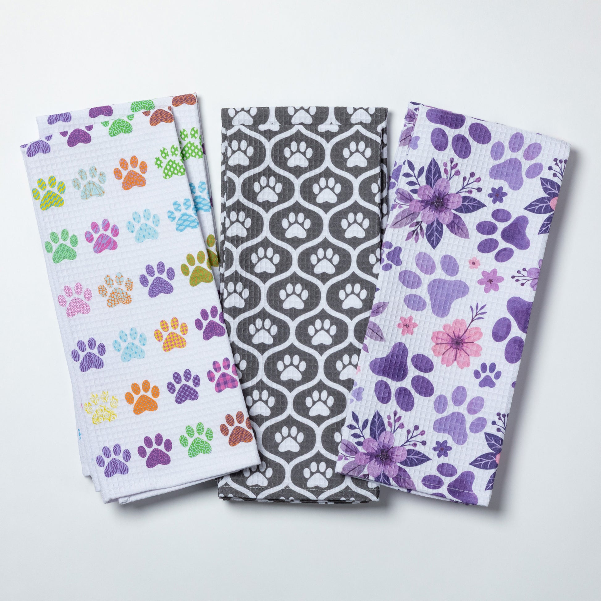 Three patterned towels with paw prints and floral designs on a white background