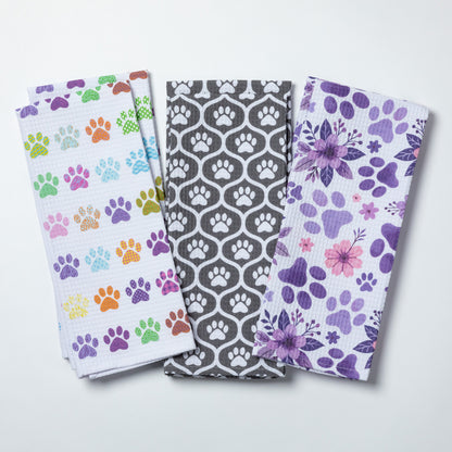 Three patterned towels with paw prints and floral designs on a white background