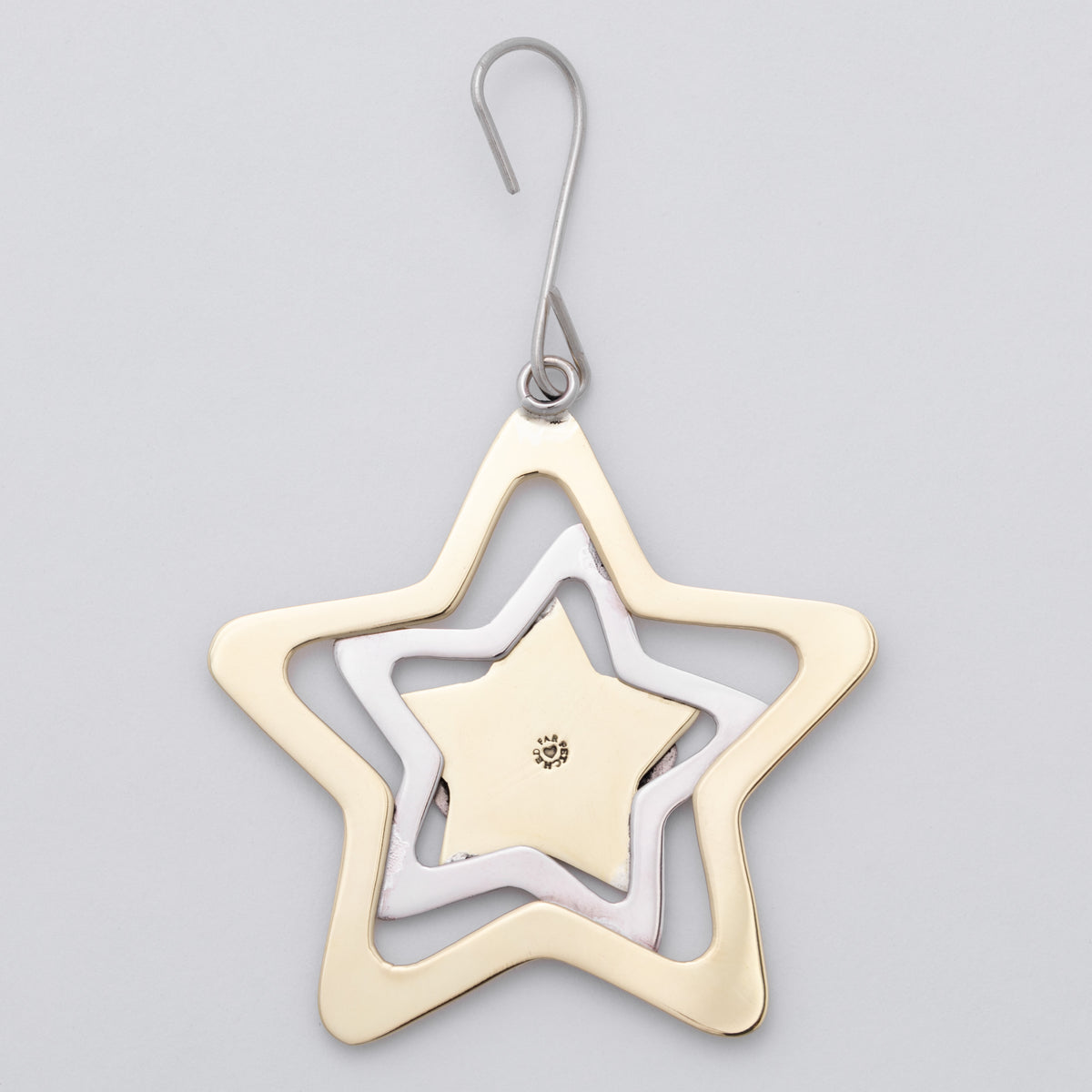A three-tiered star-shaped ornament in gold, silver, and white gold, suspended from a silver hook on a light gray background.