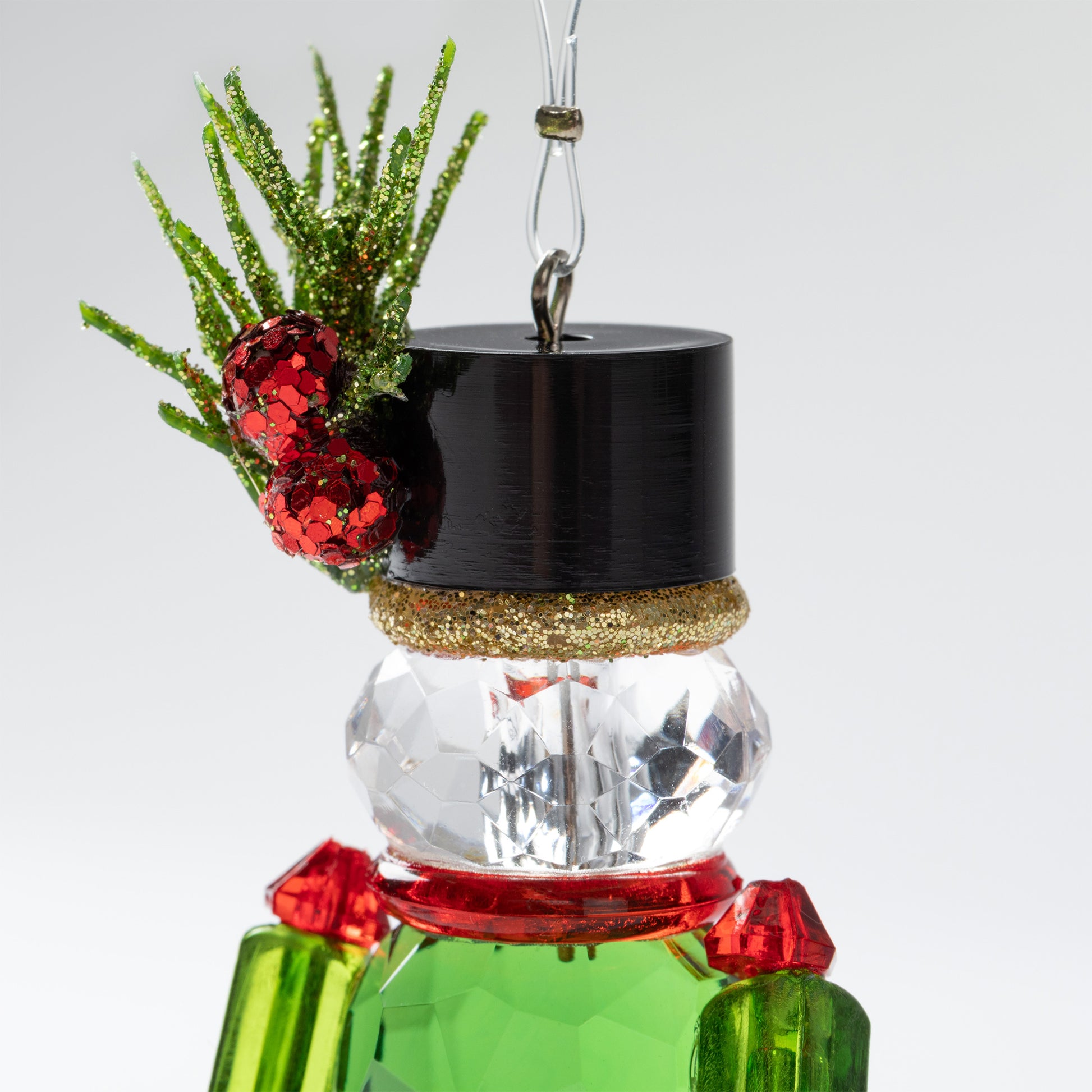 Closeup of Decorative nutcracker ornament with green body, and black top hat on a white background