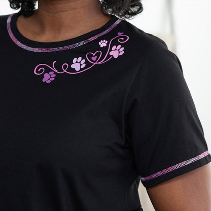 Close up of a black tee with purple contrast stitching throughout and a pink and purple paw and heart design at the neckline.