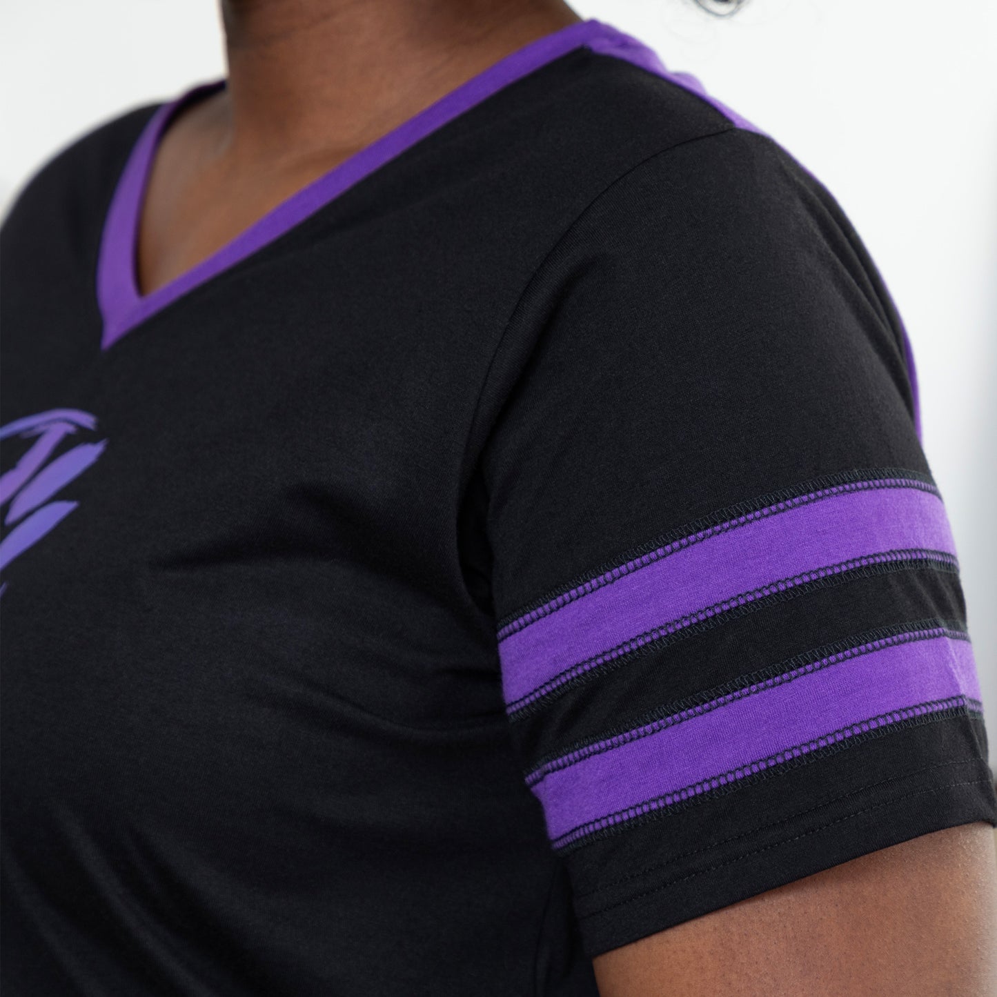 Person wearing a black t-shirt with purple athletic stripes on the sleeves on a plain  white background.
