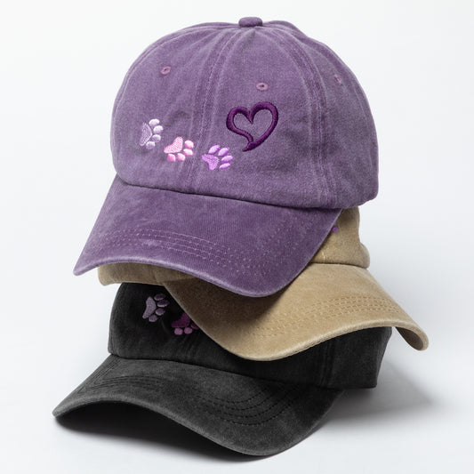 Purple baseball cap with paw prints and a heart design on a white background
