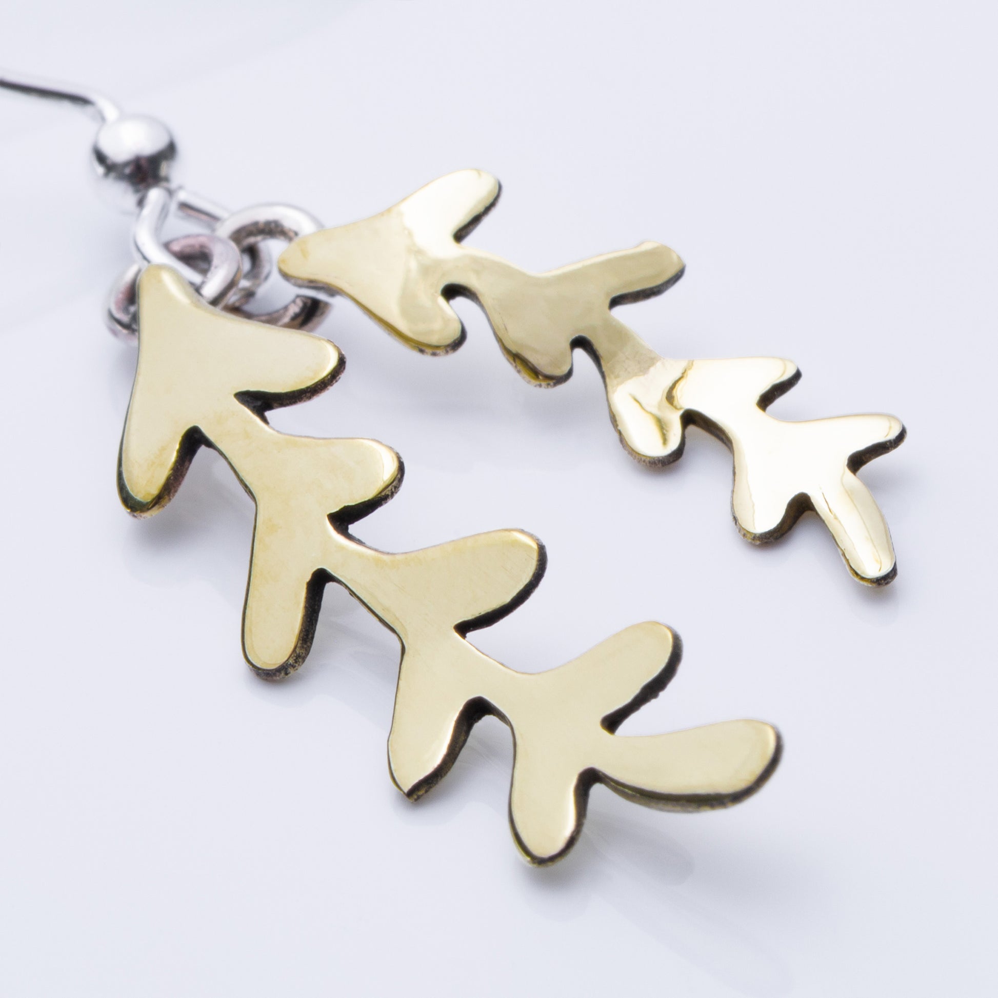 Close up of brass leaf-shaped earrings on a light gray background