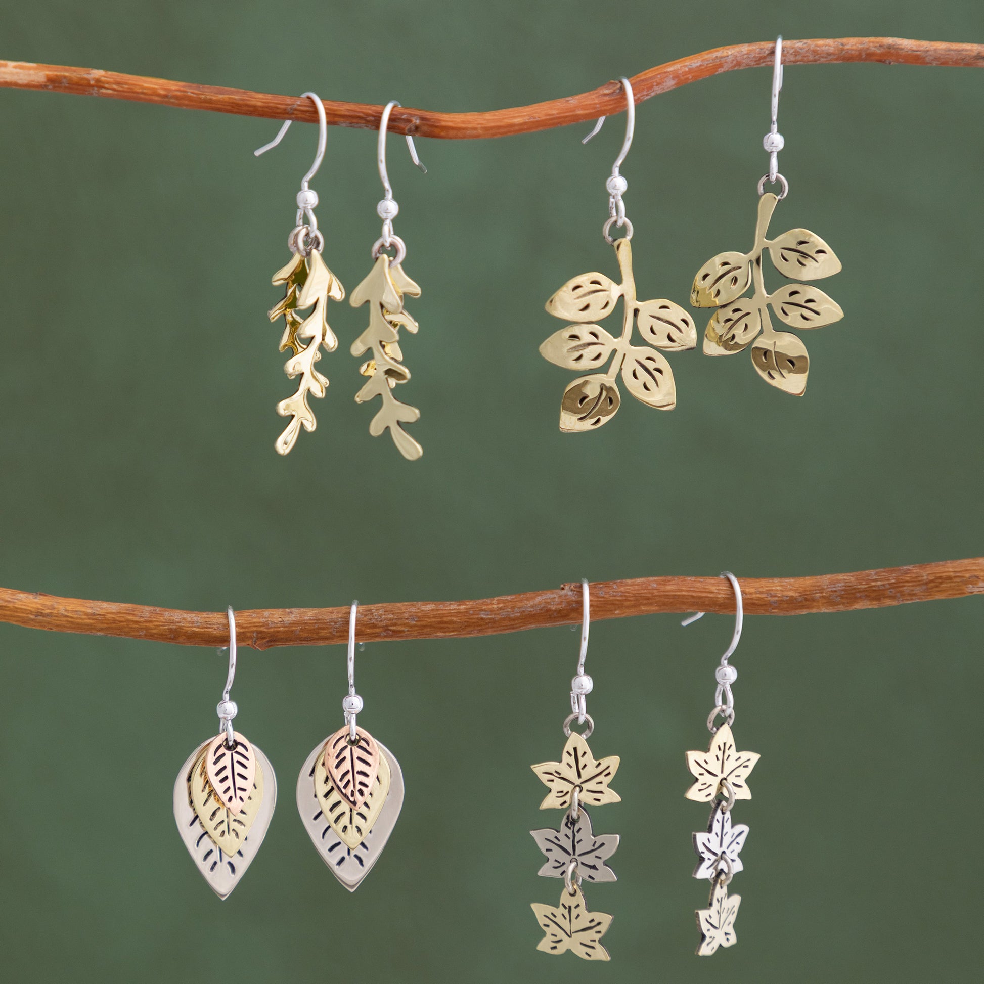 Pairs of leaf-shaped earrings on a branch against a green background