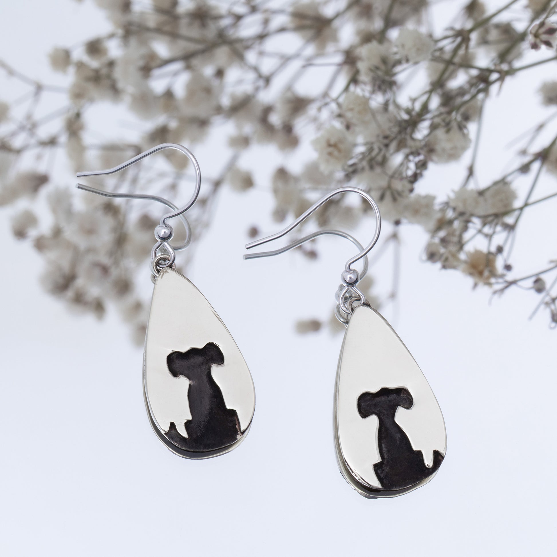 Teardrop-shaped silver earrings with black silhouette of a dog on a white background