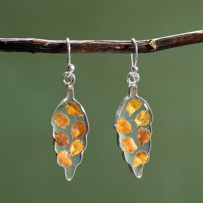 Silver earrings with leaf-shaped designs featuring embedded yellow and brown leaves on a green background.